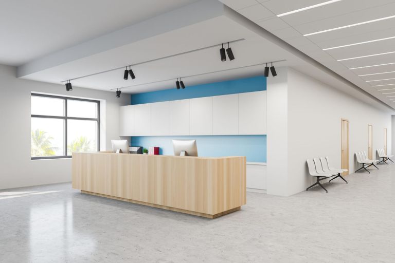 Corner of modern hospital corridor with white and blue walls, concrete floor and wooden reception desk with computers. Rows of chairs near doors. Concept of healthcare. 3d rendering