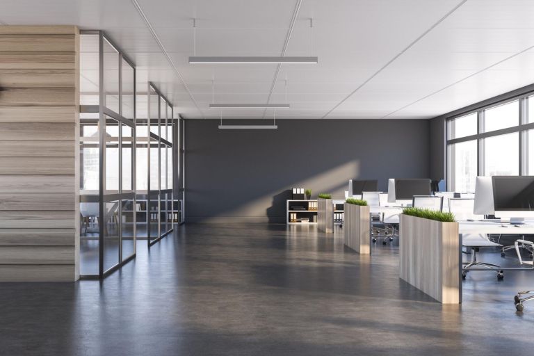 Interior of modern office with grey walls, dark concrete floor, rows of computer tables with flower beds and panoramic windows. 3d rendering